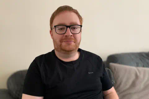 一个留着红色头发和胡须的男人穿着黑色T恤凝视着镜头